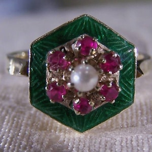 May include: A gold ring with a green enamel hexagonal setting. The setting is decorated with a cluster of pink gemstones and a single white pearl in the center.