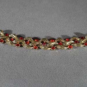 May include: A gold-tone bracelet with a chain-link design and red rhinestone accents.