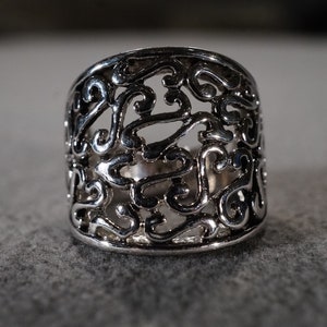 May include: A silver filigree ring with a wide band and intricate design.