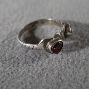 May include: A silver ring with two red gemstones set in the band. The ring has a textured design on the band.