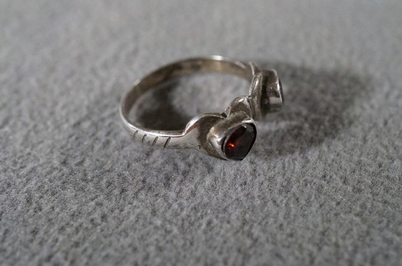 May include: A silver ring with two red gemstones set in the band. The ring has a textured design on the band.