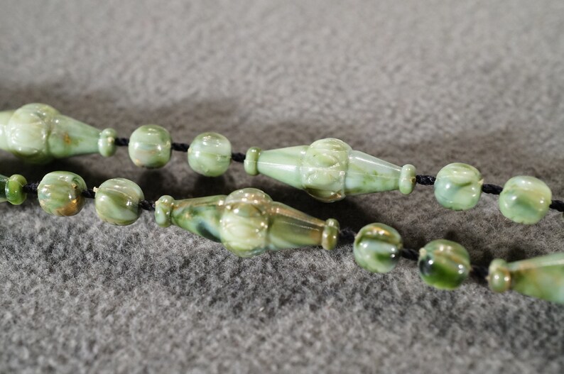 May include: A green and gold glass bead necklace with a black cord. The beads are round and have a marbled pattern.