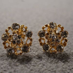 May include: A pair of gold earrings with a floral design and clear rhinestones.