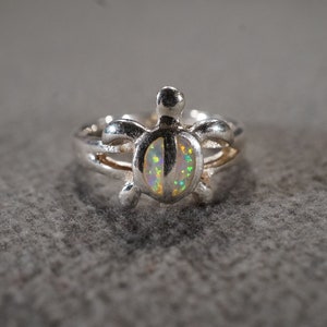 May include: A silver ring with a turtle design featuring an iridescent opal gemstone.