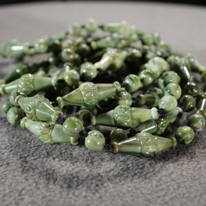 May include: A strand of green jade beads with intricate carvings, strung on black cord.