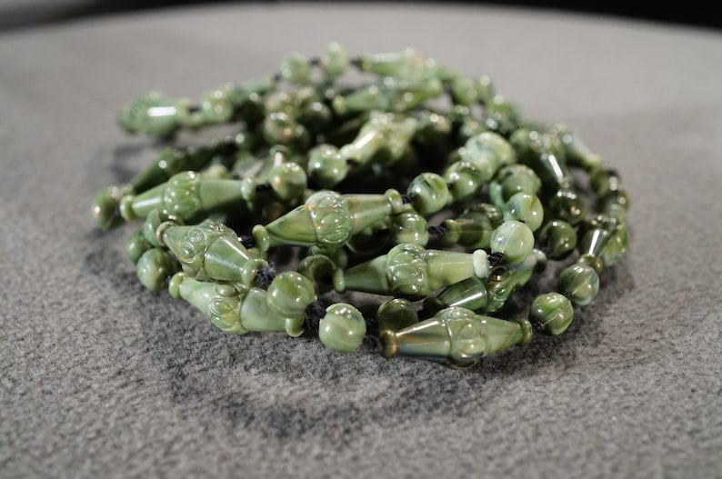May include: A strand of green jade beads with intricate carvings, strung on black cord.