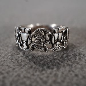 May include: A silver ring with a detailed design featuring a skull, a flower, and other intricate elements.