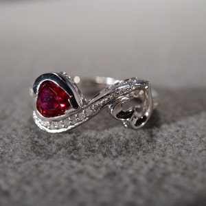 May include: A silver ring with a heart-shaped ruby gemstone and smaller diamonds set in the band.