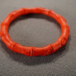 May include: A red carved bamboo bangle bracelet. The bracelet is made of multiple pieces of bamboo that have been carved with a floral design.