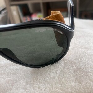 May include: Black sunglasses with a brown leather nose pad and the text "Wayfarer" on the frame.
