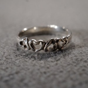 May include: A silver ring with a design of four interlocking hearts.