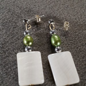 May include: A pair of white rectangular earrings with green and silver beads.