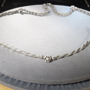 May include: A silver chain necklace with five small, round, clear crystal accents. The chain is twisted and has a delicate, feminine look.