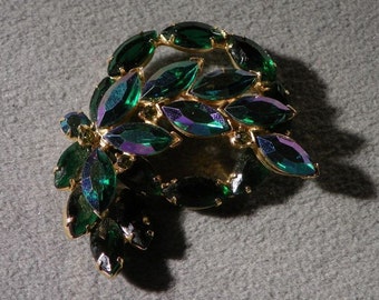 May include: A gold-toned brooch with a cluster of iridescent green leaves. The leaves are arranged in a swirling pattern and have a slightly textured surface.