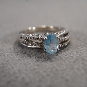 May include: A silver ring with a light blue oval gemstone set in the center. The ring has a delicate design with small diamonds on the band.