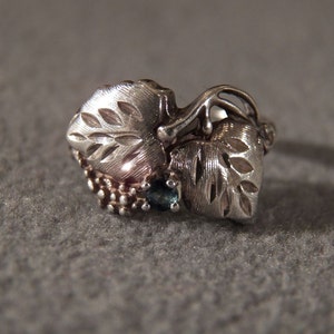 May include: A silver ring with a leaf design and blue gemstones. The ring is made of metal and has a delicate, intricate design.