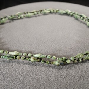 May include: A green and black beaded necklace with a long, thin, and slightly curved shape. The beads are made of a smooth, polished material and have a subtle sheen.