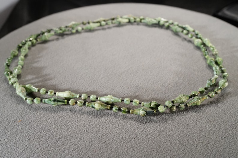 May include: A green and black beaded necklace with a long, thin, and slightly curved shape. The beads are made of a smooth, polished material and have a subtle sheen.