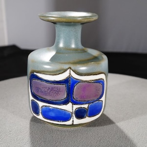 May include: A small, blue and purple ceramic vase with a geometric design. The vase has a narrow neck and a wide base.