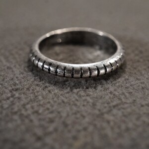 May include: A silver ring with a textured band. The band has a series of raised lines that run around the entire ring.