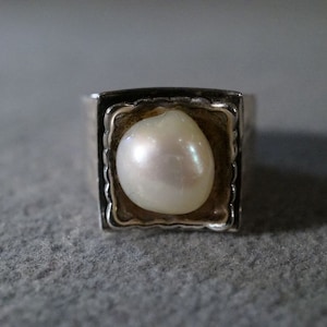 May include: A silver ring with a square setting featuring a white pearl.