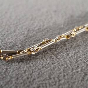 May include: A close-up of a silver and gold chain necklace. The chain is made of alternating silver and gold links.