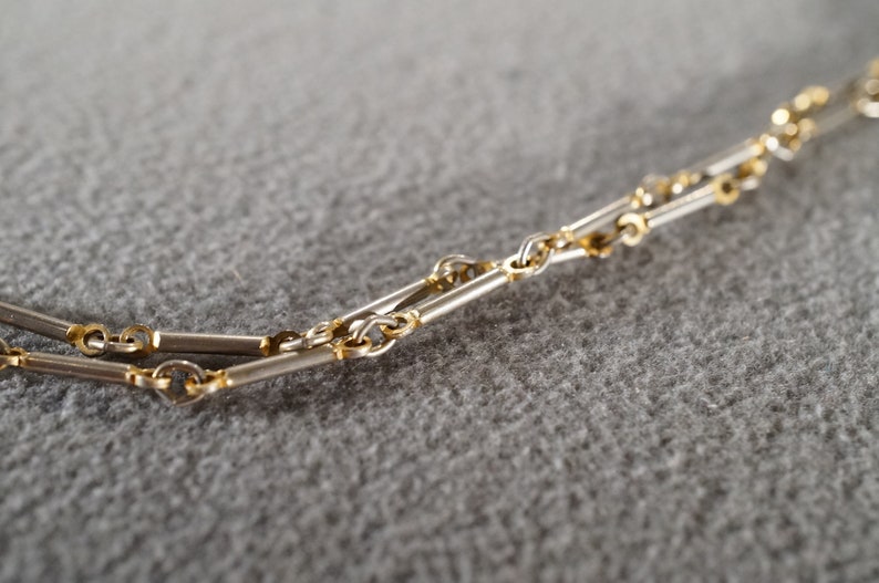 May include: A close-up of a silver and gold chain necklace. The chain is made of alternating silver and gold links.