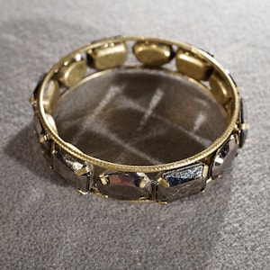 May include: A gold bangle bracelet with black faceted stones. The bracelet is made of metal and has a simple design.