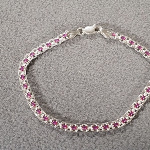 May include: A silver bracelet with a row of pink gemstones.