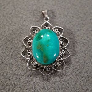 May include: A silver pendant with a green gemstone set in a filigree design.