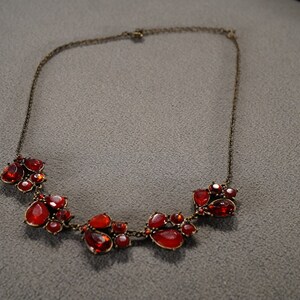 May include: A red gemstone necklace with a cluster of red stones in the center. The necklace is made of a thin gold chain.