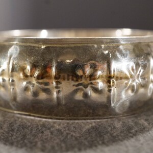 May include: A silver ring with a textured design of repeating floral patterns.