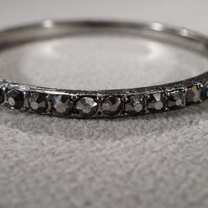 May include: A silver bangle bracelet with a row of black rhinestones.
