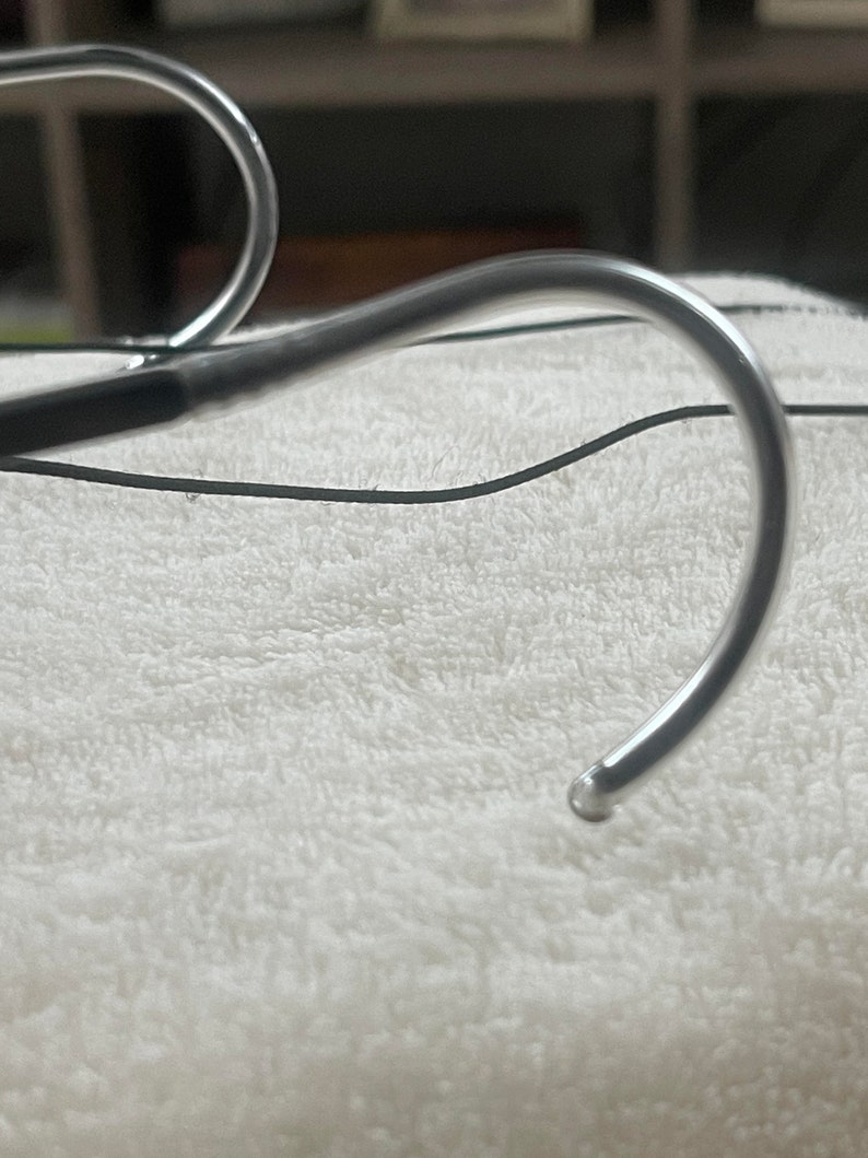 May include: Close-up of a silver medical device with a curved, hook-like end. The device is lying on a white, fluffy surface.