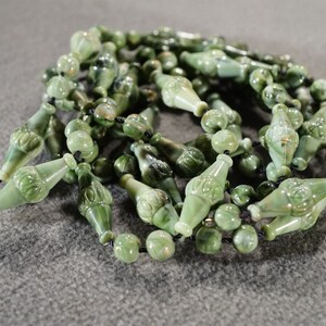 May include: A long strand of green jade beads with carved details. The beads are strung on a black cord.