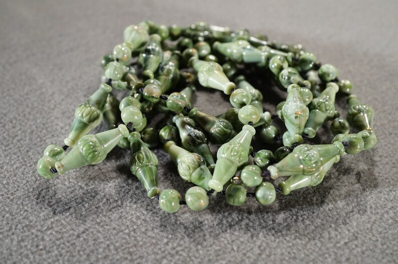 May include: A long strand of green jade beads with carved details. The beads are strung on a black cord.