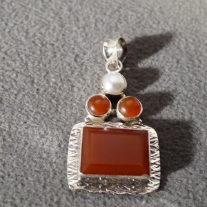 May include: A silver pendant with a rectangular carnelian stone surrounded by three smaller carnelian stones and a white pearl.