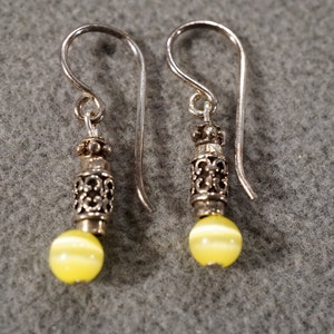 May include: A pair of silver earrings with yellow cat's eye beads and filigree detailing.