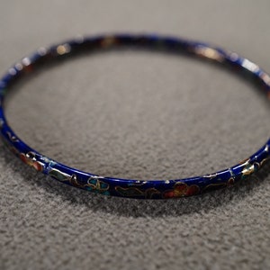 May include: A blue bangle bracelet with a floral design in gold, red, and blue.