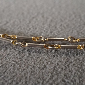 May include: A silver and gold chain necklace with a box chain design. The chain is made of two different metals, with silver links alternating with gold links.