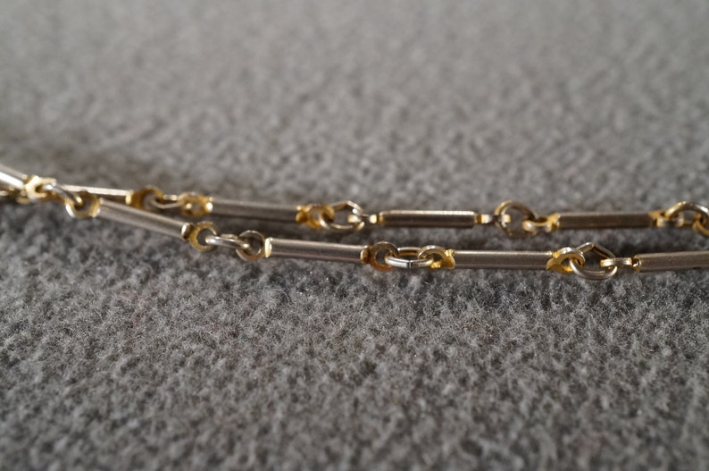 May include: A silver and gold chain necklace with a box chain design. The chain is made of two different metals, with silver links alternating with gold links.