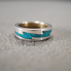May include: A silver ring with a turquoise inlay in the shape of a lightning bolt.