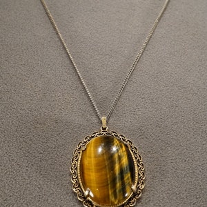 May include: A gold chain necklace with a large oval-shaped tiger's eye pendant set in a gold filigree frame.