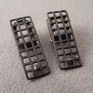 May include: A pair of black metal earrings with a geometric grid design.