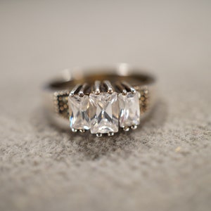 May include: A silver ring with three clear rectangular stones set in the center.