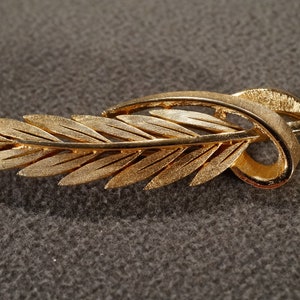 May include: A gold-toned leaf-shaped brooch with a twisted stem.