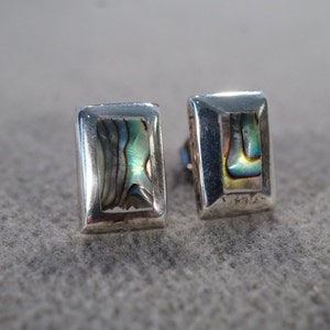 May include: A pair of silver earrings with rectangular abalone shell insets. The earrings have a silver backing.