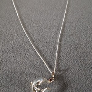 May include: A silver chain necklace with a silver dolphin pendant featuring a red gemstone.
