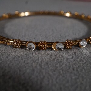 May include: A gold bangle bracelet with clear rhinestones and a beaded design.