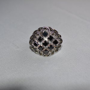 May include: A silver ring with a black stone design. The ring has a filigree pattern and is set with multiple black stones.